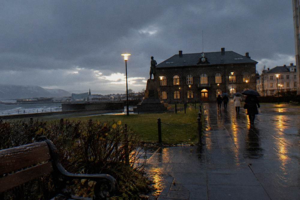 A rainy Reykjavik street with wet pavement reflecting streetlights in late afternoon darkness