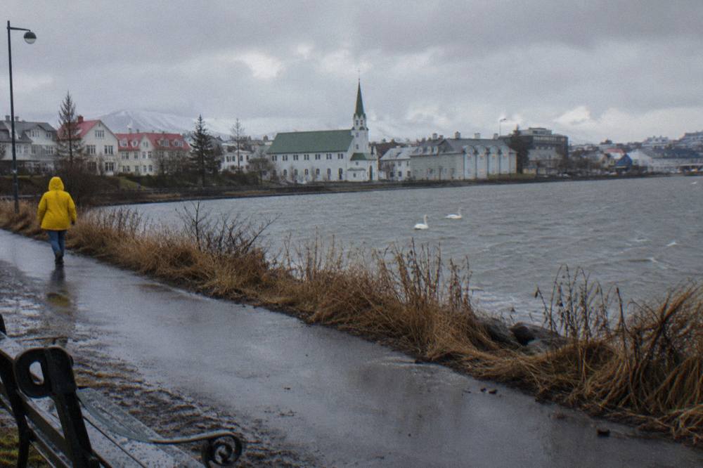 Person walking a Reykjavik sidewalk in light rain wearing a waterproof jacket