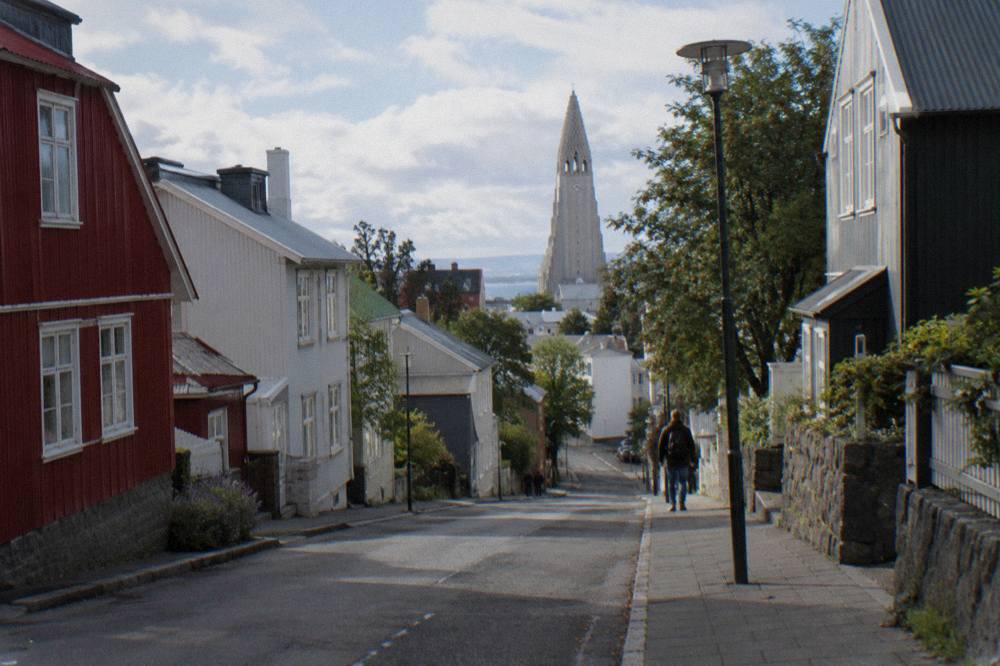 A low-rise city centre street with colourfully painted houses and a church tower in the background