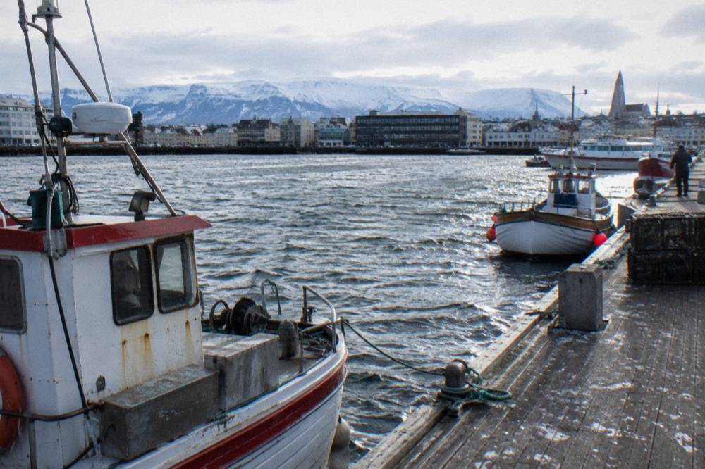 Moored boats and a wooden dock along a small harbour with a mountain ridge behind