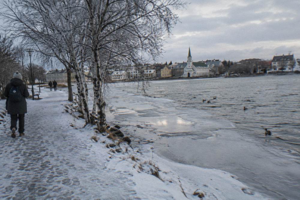 A snow-dusted park path beside a frozen city pond in low winter light