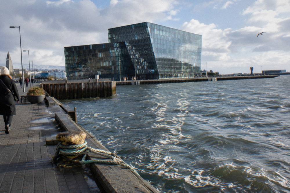 The glass facade of the Harpa concert hall seen from the harbour promenade on a bright afternoon