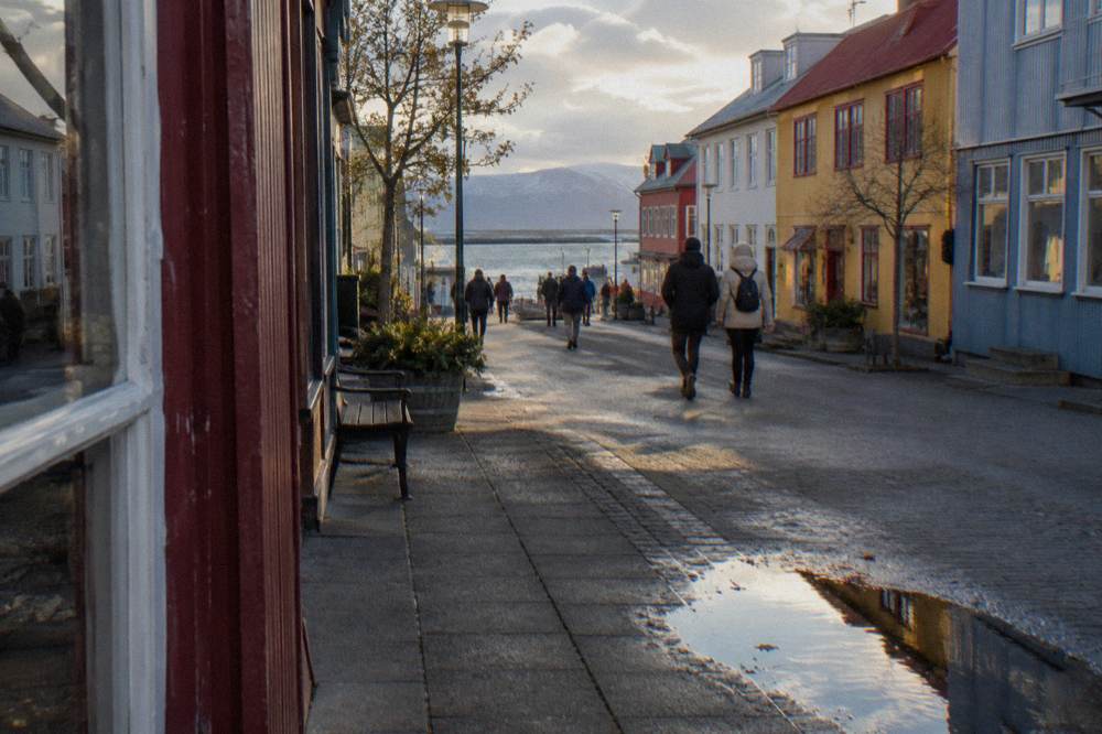 People walking along Laugavegur shopping street past storefronts with the afternoon sun low over the rooftops