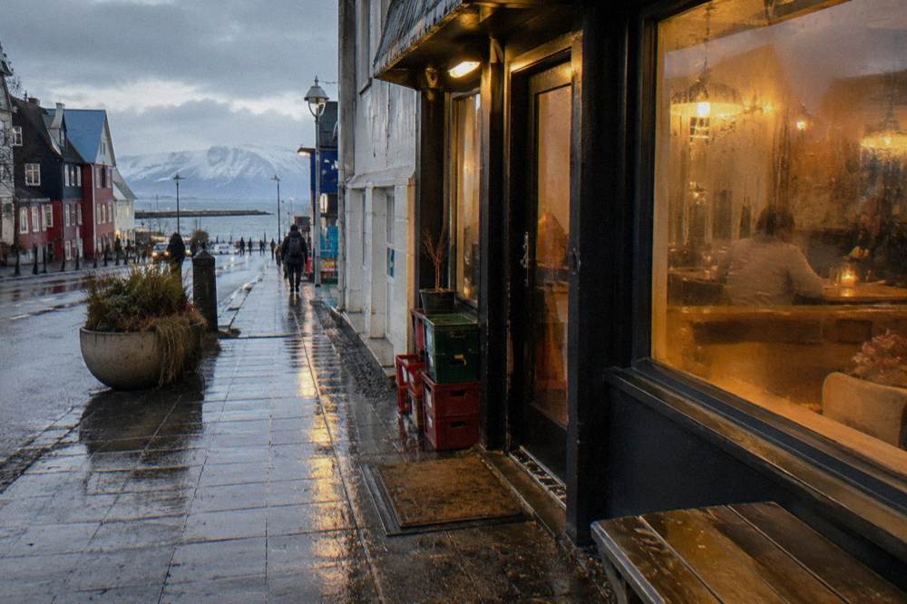 Warm light glowing from restaurant windows on a wet Reykjavik street in the evening
