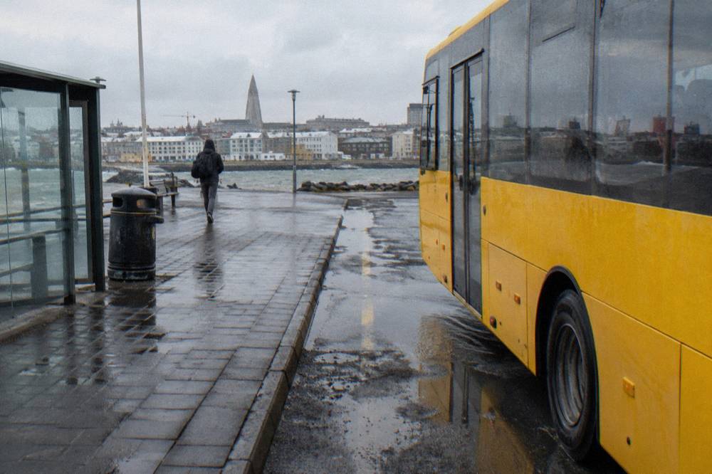 A city bus parked at a stop beside a wet street in low daylight