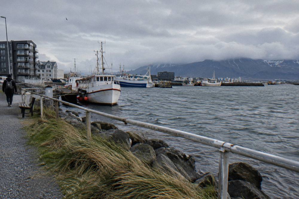 Waterfront walking path along Reykjavik harbour with moored boats and low clouds