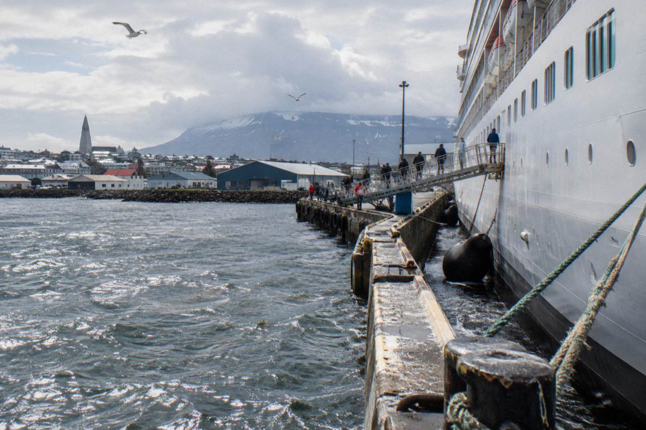 Cruise ship moored at a Reykjavik harbour pier with low buildings and hills beyond