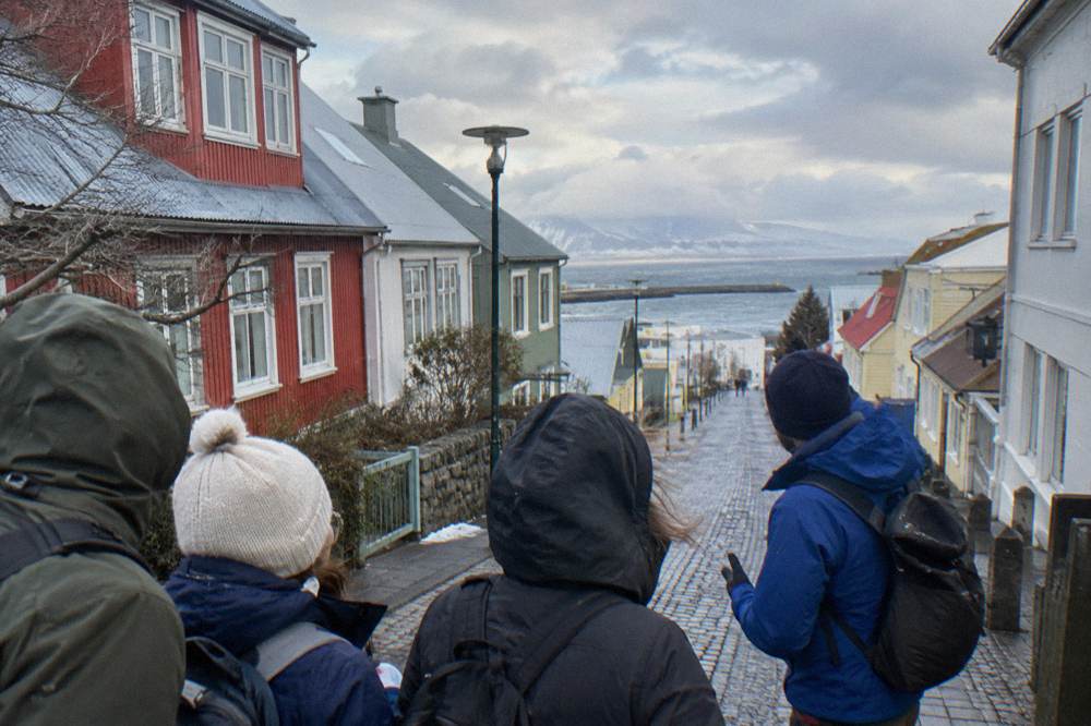 A small group of waterproof jacketed walkers gathered around a guide on a cobblestone pedestrian street