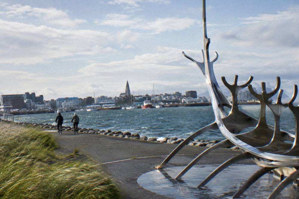 Cyclists on a flat coastal path beside Reykjavik harbour with moored boats