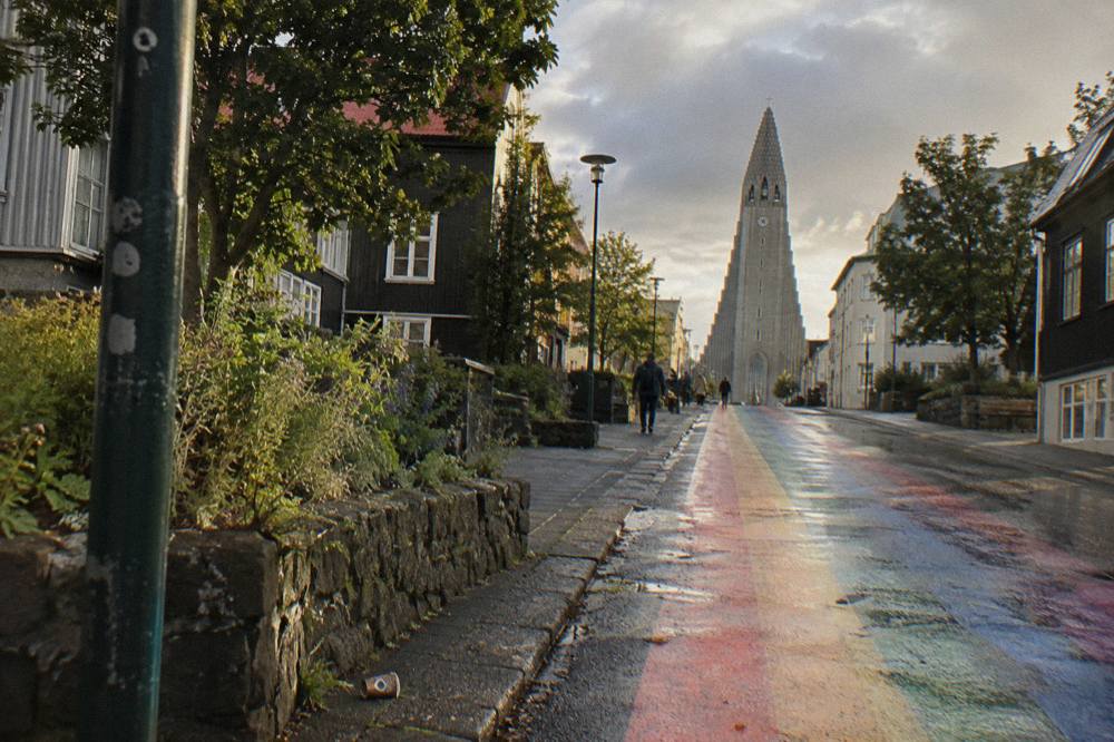 Rainbow painted street rising toward a tall grey stone church