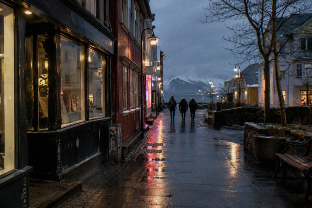 People in winter coats and knit hats walking along an illuminated shopping street at night