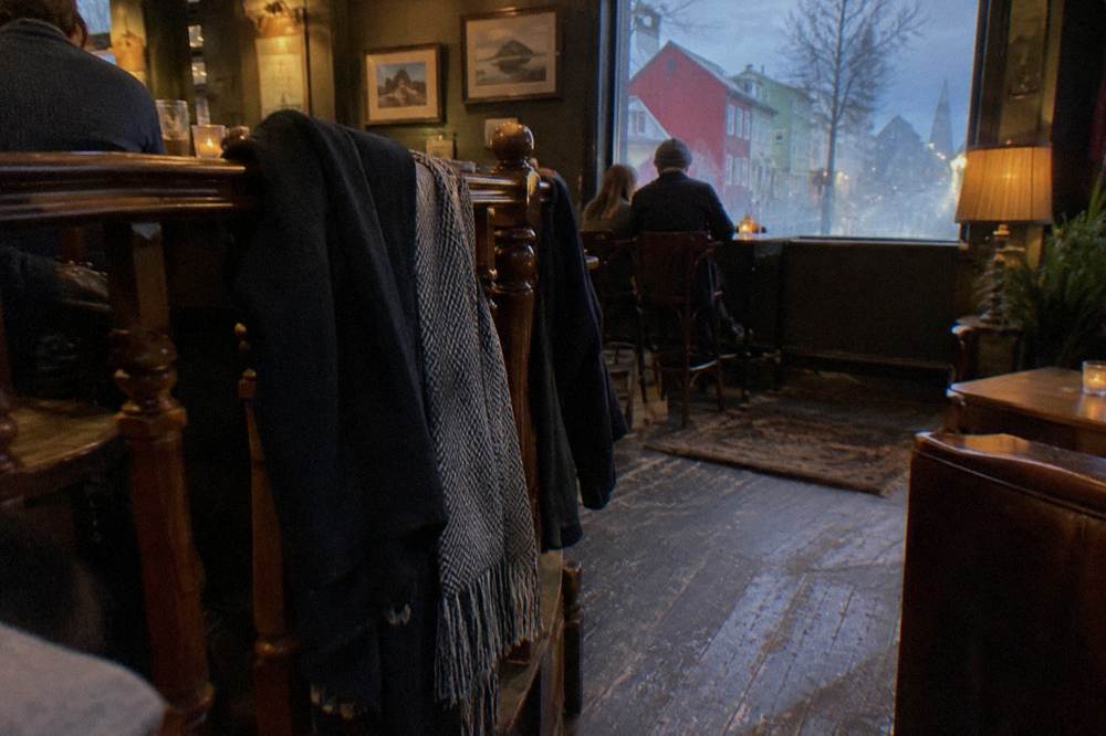 A row of dark coats and scarves hung along a wooden railing inside a warmly lit bar