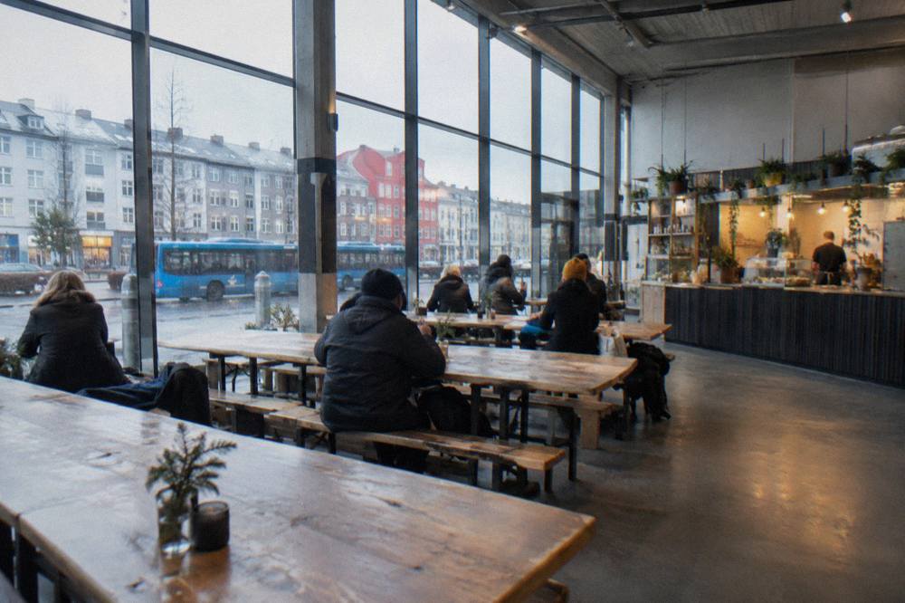 Interior of a bright food hall with long communal wooden tables and vendor counters along one wall