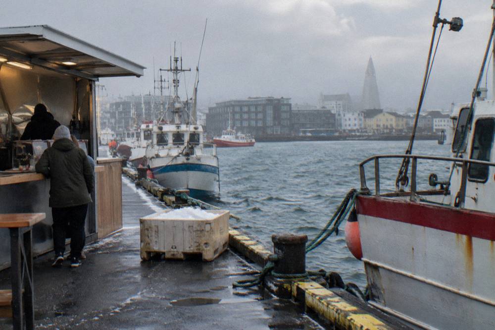 Small harbour street with a food stand counter and fishing boats moored along the pier