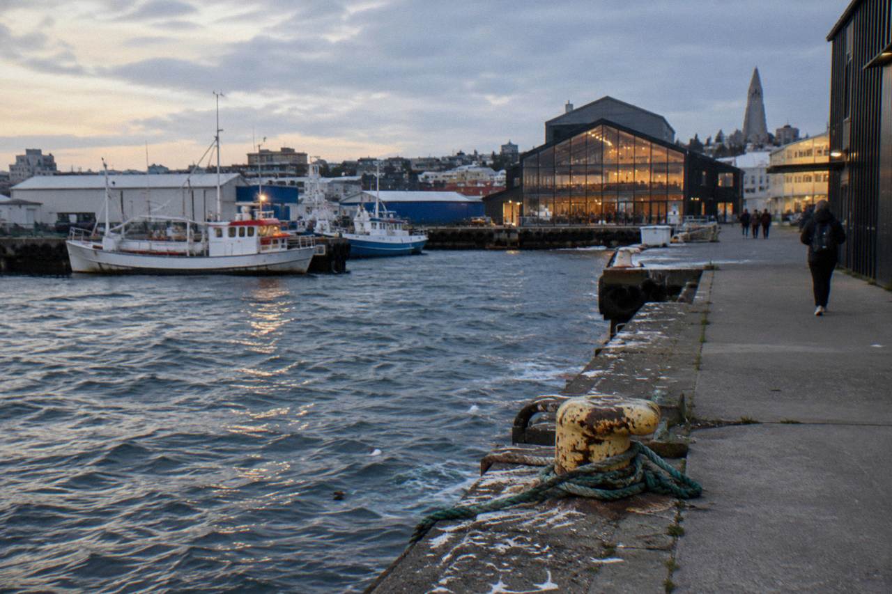 Evening light over a small harbour district street with a food hall entrance and fishing boats moored behind
