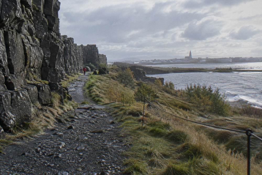 Thingvellir rift valley path with rocky cliffs and a still lake in the distance