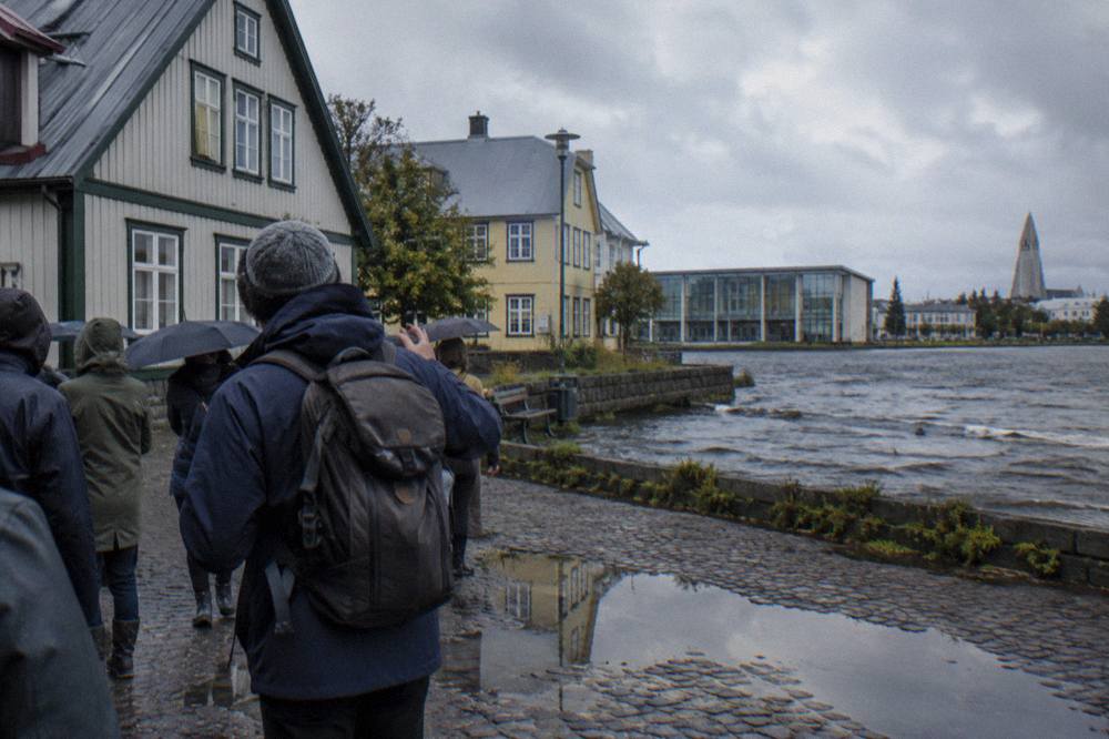 A guide speaking to a small group on a cobblestone square beside old timber buildings in central Reykjavik