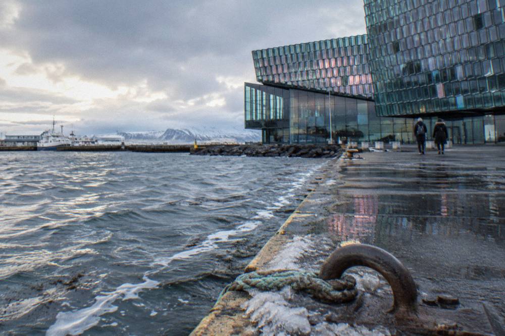 The glass facade of the Harpa concert hall reflecting low winter light beside the old harbour