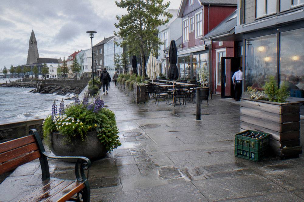 A narrow downtown street lined with shops and cafes under a bright overcast sky