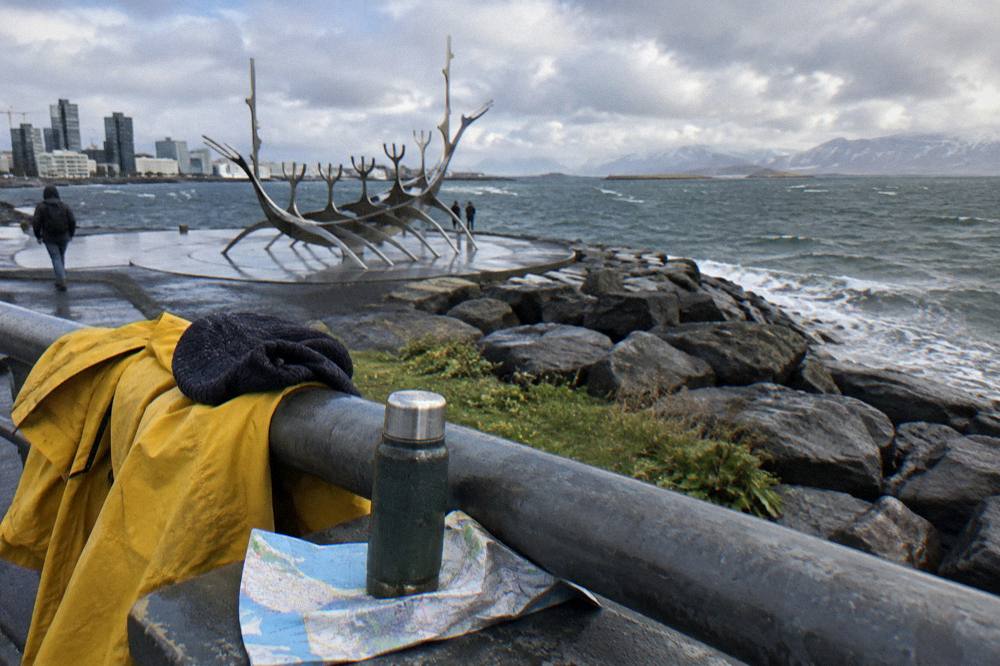 Waterproof jacket and wool hat resting on a boat rail with grey sea and low islands behind