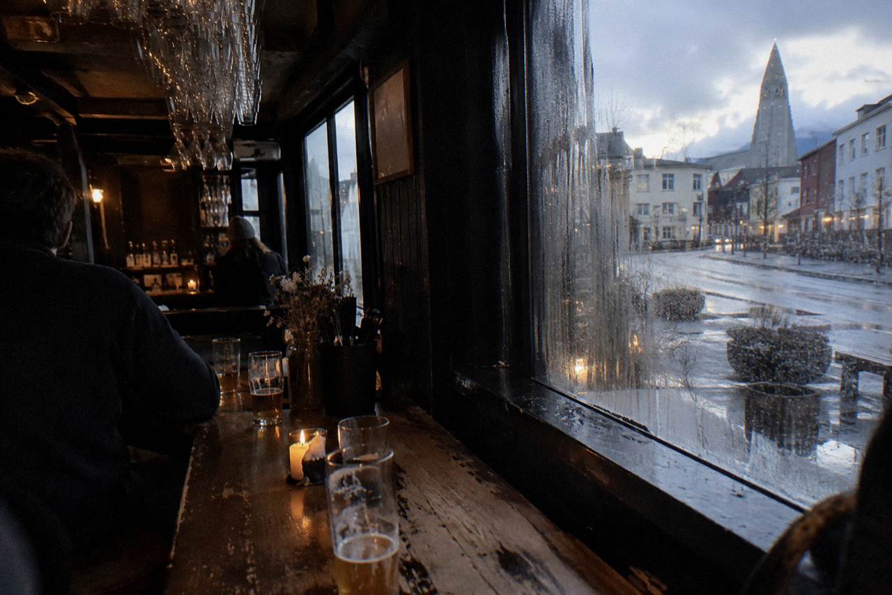 Dimly lit craft beer bar interior in downtown Reykjavik with rows of glasses on a wooden counter