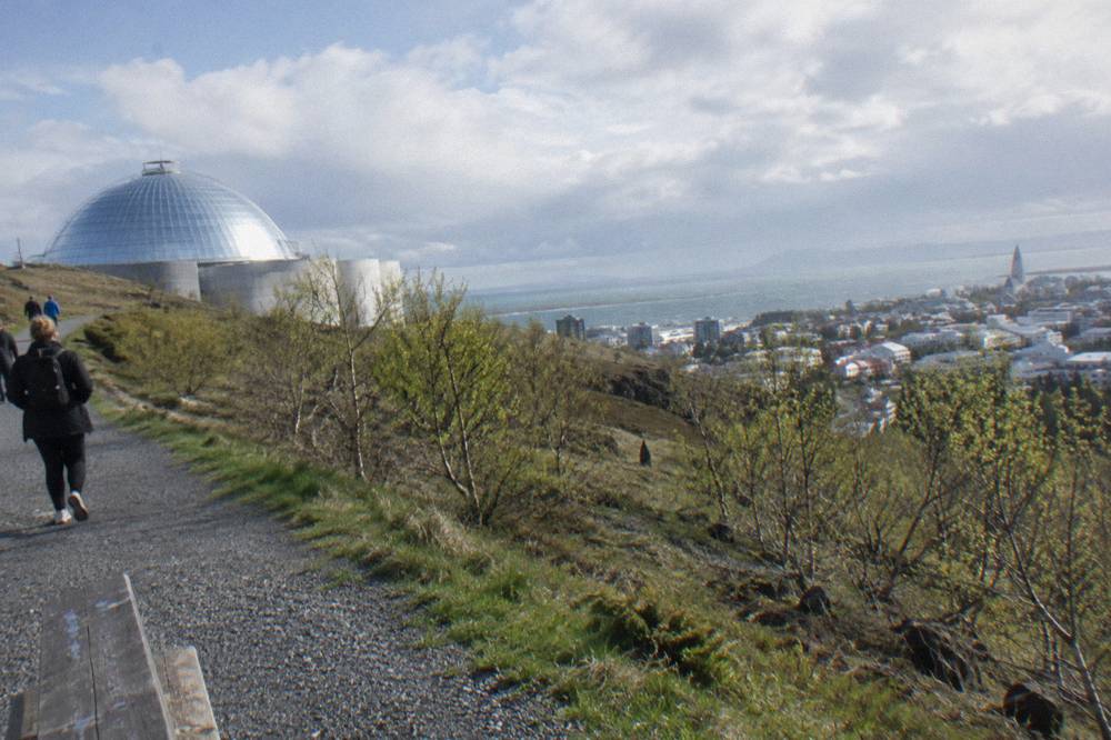 Electric bicycles parked on a gravel path at the edge of a green hillside above Reykjavik