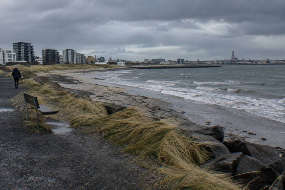 Empty cycle path along the Reykjavik shoreline under a wide grey sky with low waves