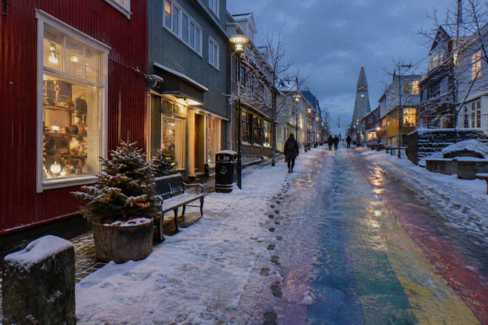 A snow-dusted pedestrian street in Reykjavik with warm light from shop windows reflecting on wet pavement