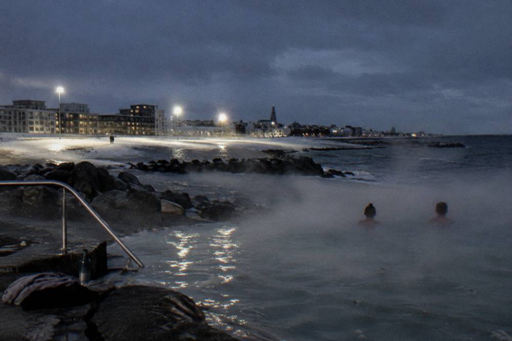 A geothermal outdoor pool in Reykjavik with steam rising into the dark winter air