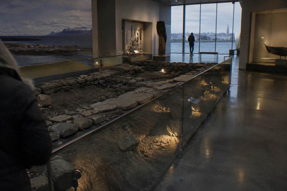 An underground museum exhibition with the stone foundations of a Viking age longhouse lit behind glass