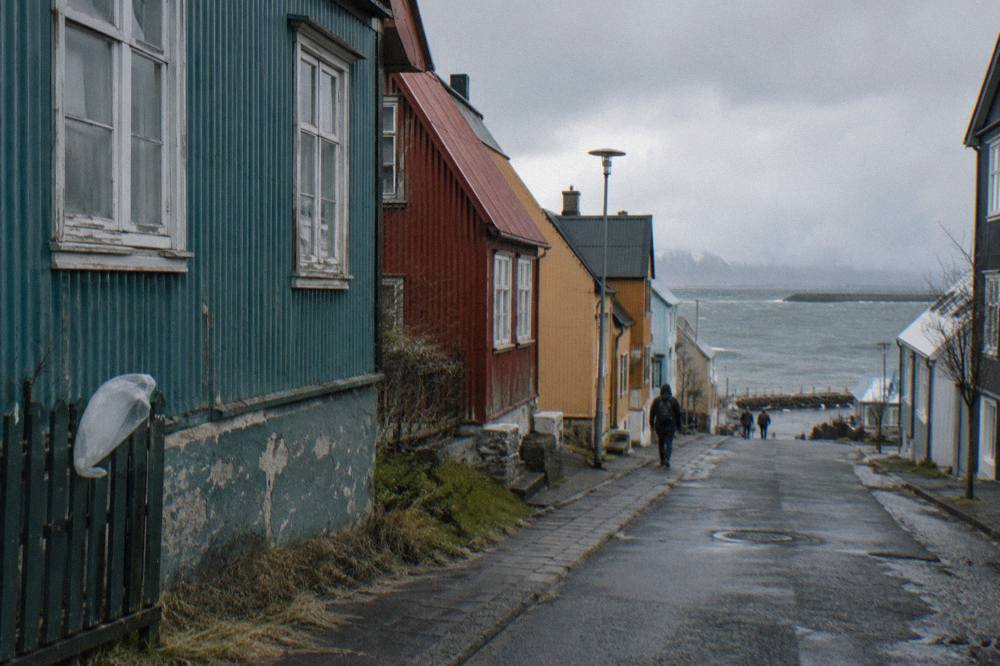 A narrow downtown street of colourfully painted corrugated iron houses under a grey sky