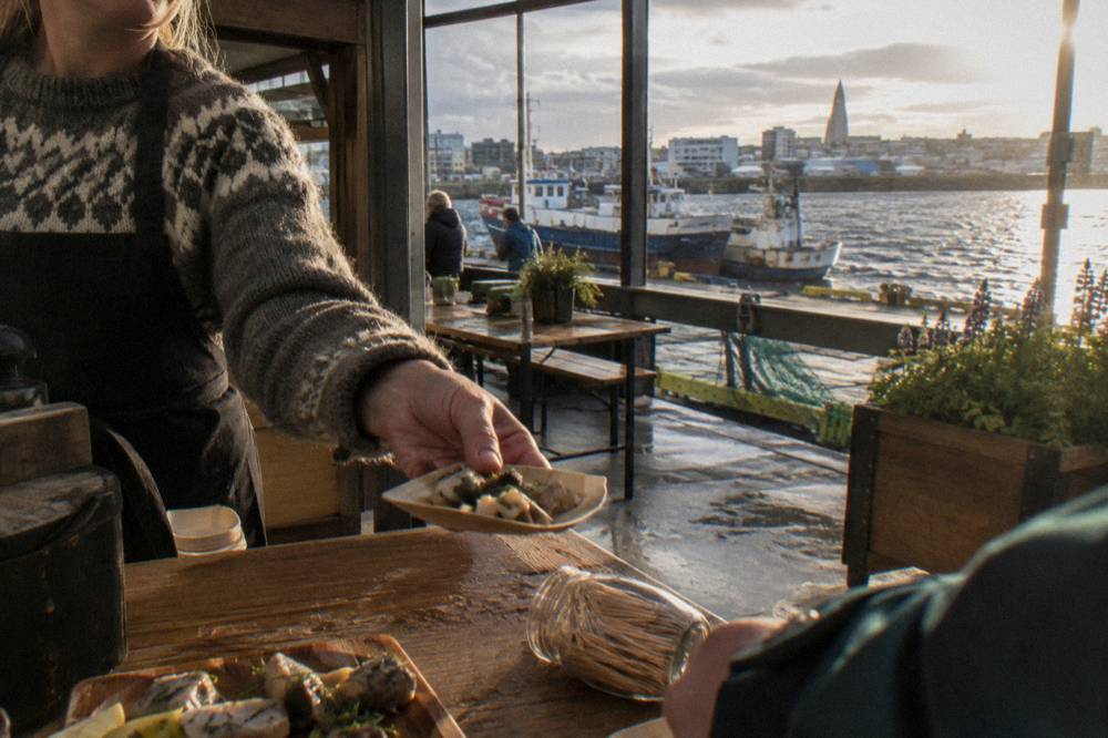 Guide handing a tasting plate to a guest at a harbour district food stall