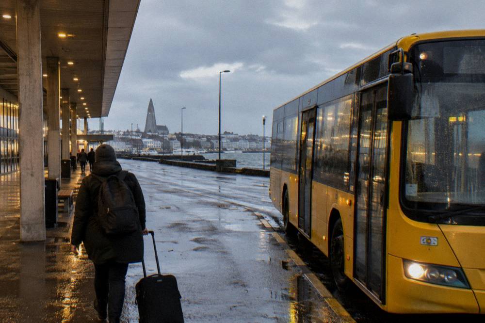 A yellow city bus at a stop on a wet Reykjavik street with rain-flecked windows