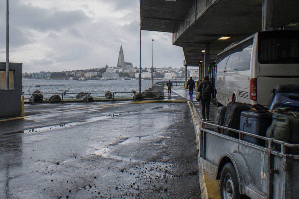 Bus parked at the Keflavik airport arrivals curb with the terminal building behind it