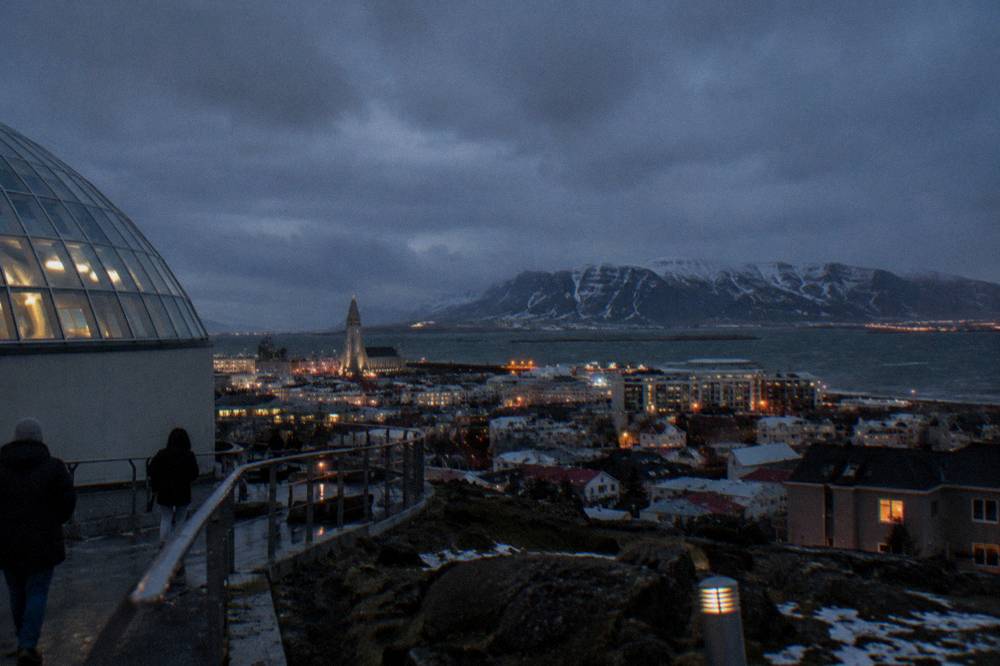 Reykjavik city rooftops under a dark winter sky with snow patches on the mountains