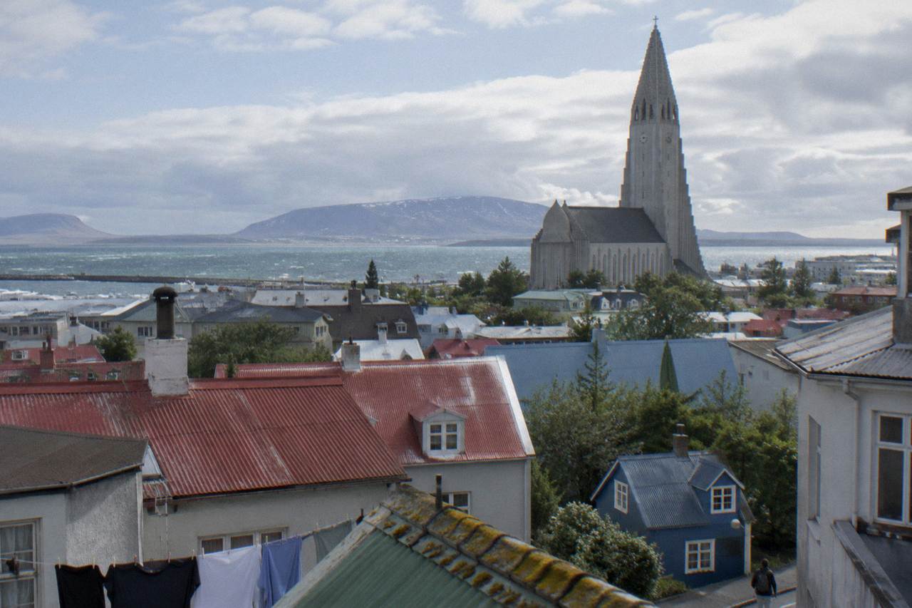 View across Reykjavik old town rooftops toward the Hallgrimskirkja church tower under a bright sky
