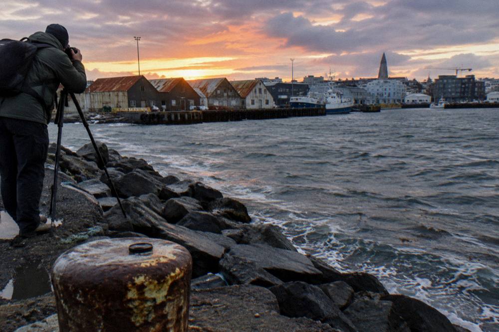 A photographer with a tripod on the harbour breakwater under a colourful dusk sky
