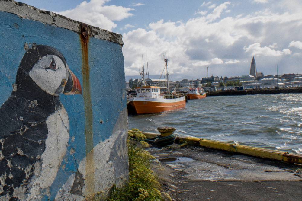 Mural on a harbour district building under a bright sky with fishing boats nearby