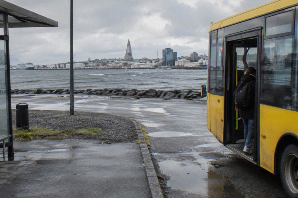 City bus parked at a Reykjavik street stop with low buildings behind