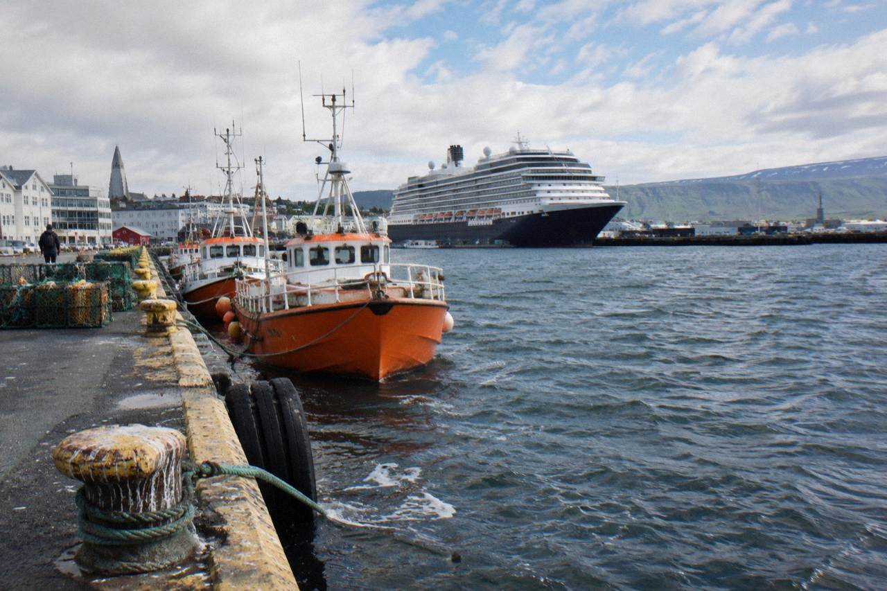 Cruise ship docked at a Reykjavik harbour with moored boats and low hills behind