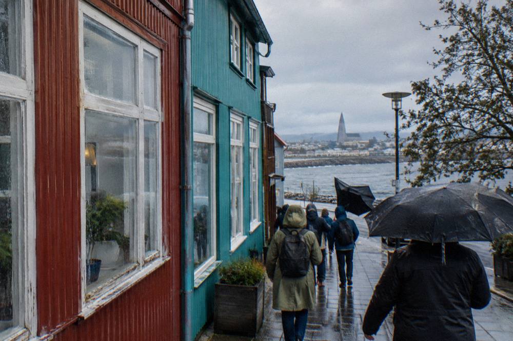 Guided walking group with umbrellas passing colorful corrugated iron houses on a rainy Reykjavik street