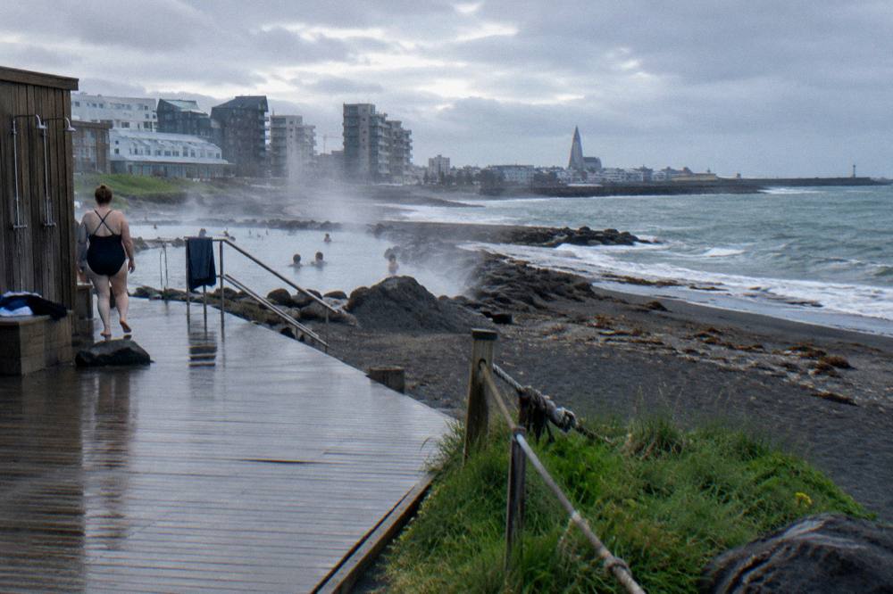 Steam rising from an outdoor geothermal pool in Reykjavik under grey rainy skies