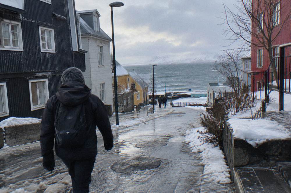 A walker in a windproof shell and wool hat crossing a snowy Reykjavik street