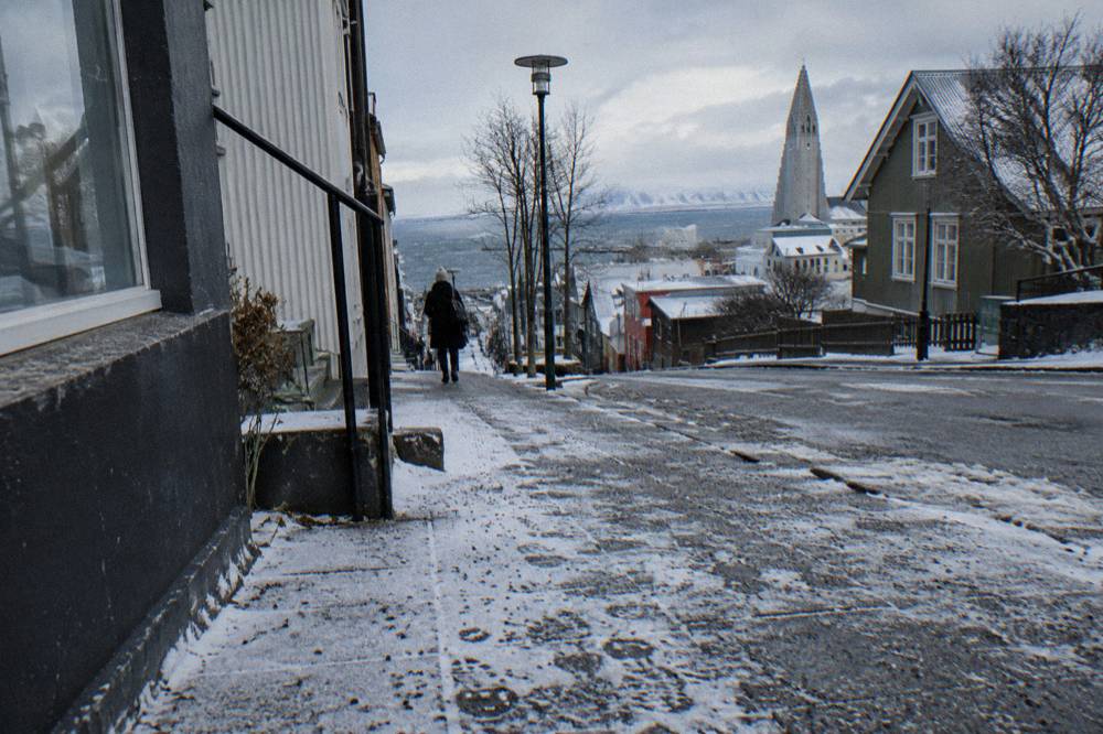 A downtown Reykjavik sidewalk dusted with snow and scattered grit under a grey sky