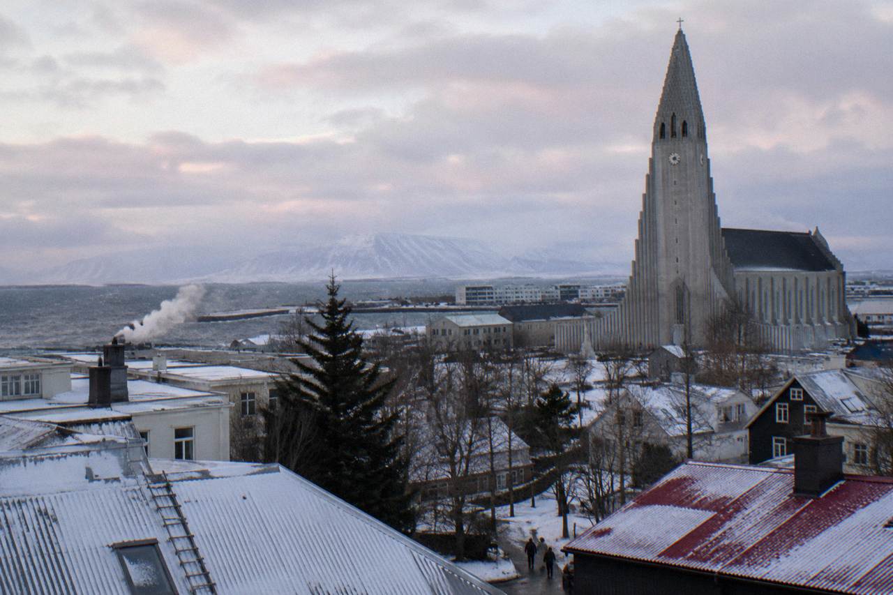 Snow dusted Reykjavik rooftops under a pale winter sky with the Hallgrimskirkja tower in the distance