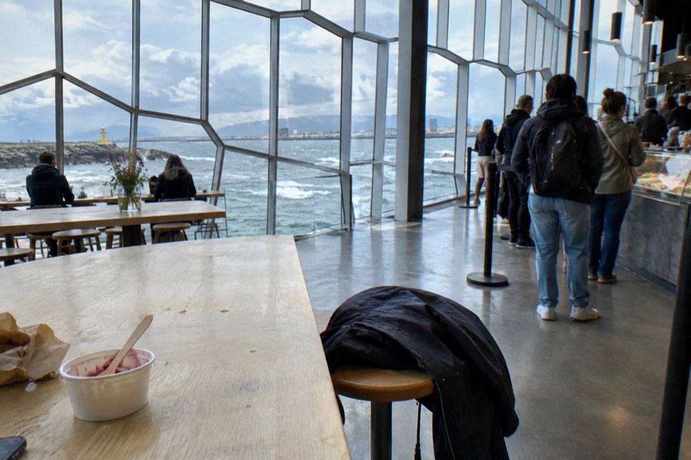 A bright food hall with communal wooden tables and people queuing at vendor counters