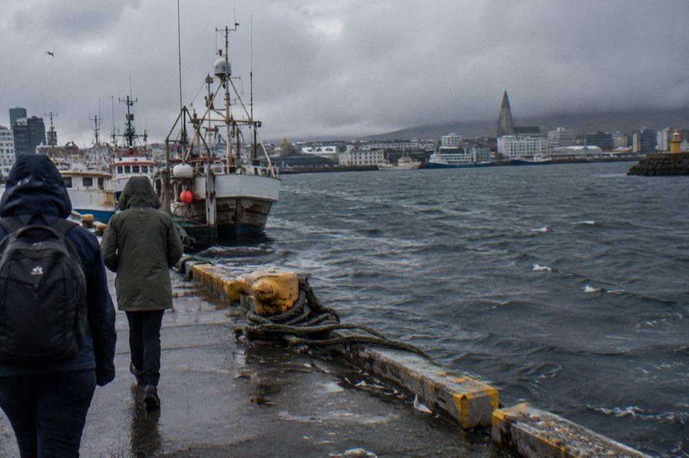 Rain jacketed visitors walking beside the old harbour in Reykjavik with moody clouds over the water