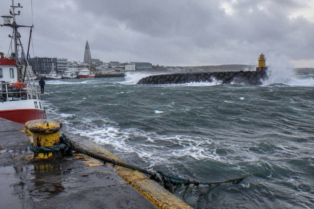 Waves breaking against the breakwater at Reykjavik old harbour under a grey windy sky