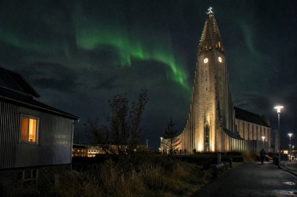 Northern lights glow above a dark Reykjavik skyline with the illuminated church tower visible