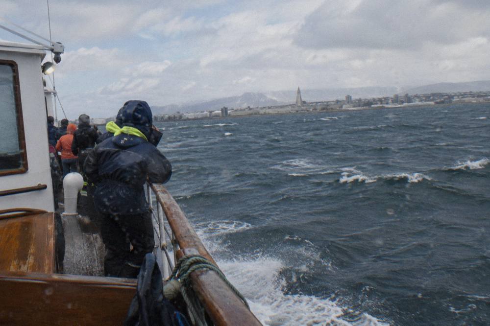 A classic whale watching ship mid-bay with passengers in overalls along the rail